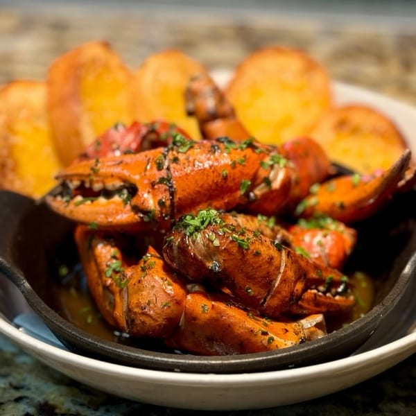 Close-up of cooked lobster claws and tails garnished with herbs, served with toasted bread.