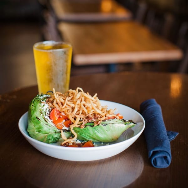 Wedge salad with crispy onions, tomatoes, and dressing, next to a glass of beer.