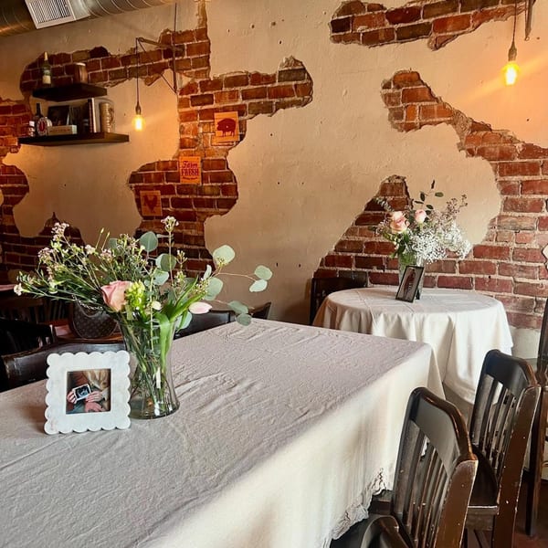 Interior of Charlies Burgers & Street Tacos with exposed brick walls, tables with tablecloths, and floral centerpieces.