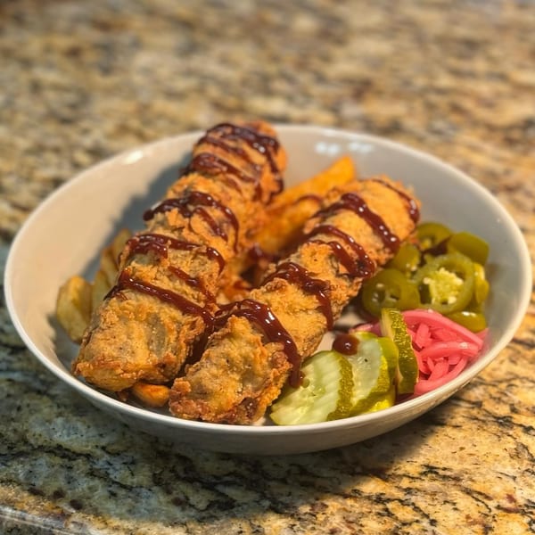 Fried chicken strips drizzled with BBQ sauce, served with fries, pickled jalapeños, and cucumbers.