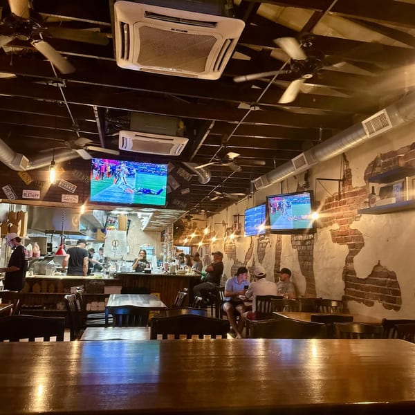Interior of Charlie's Burgers & Street Tacos with customers, staff, TVs, and exposed brick walls.