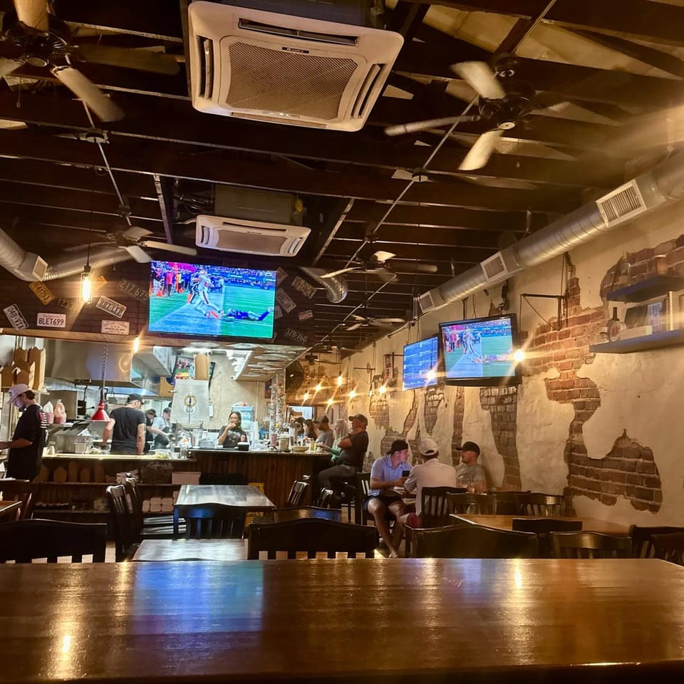 Interior of Charlie's Burgers & Street Tacos with customers, staff, TVs, and exposed brick walls.