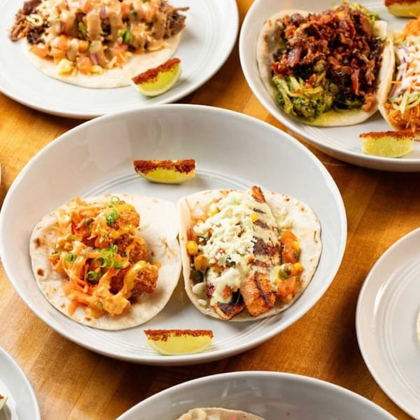 Multiple plates of Charlies Burgers & Street Tacos, including crispy shrimp and grilled chicken tacos.