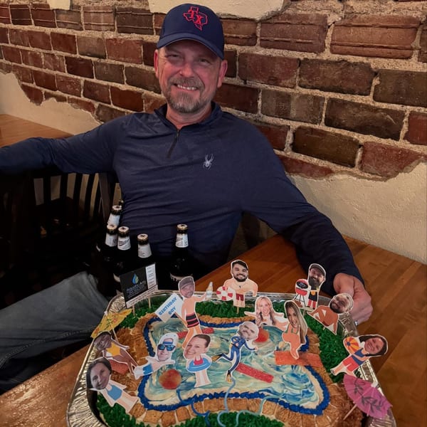 A man in a Texas hat smiles behind a pool-themed birthday cake with photo cutouts of people.